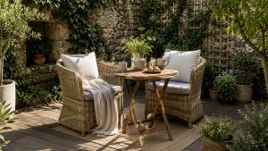 Small garden patio with a cozy wicker bistro set, wooden table, soft neutral cushions, coffee table styling, natural greenery, and warm sunlight creating a peaceful outdoor atmosphere.